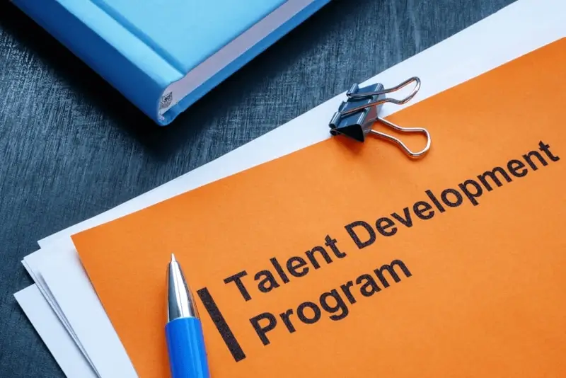 A stack of paper lies on a desk titled 'Talent Development Program'