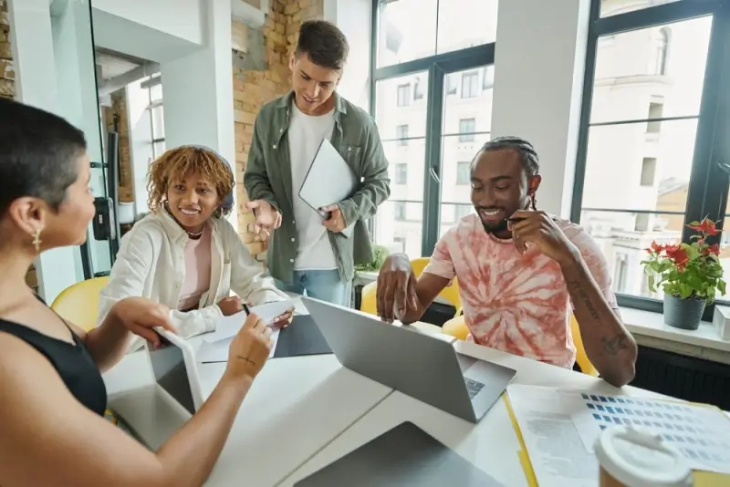 Four smiling people discuss work around a table